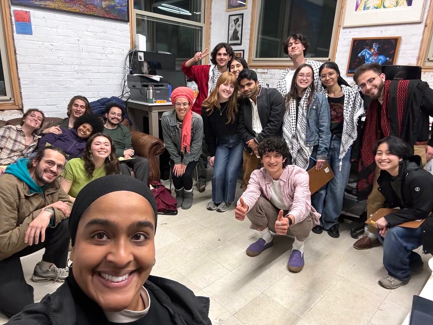 A group of people sit on a couch and kneel on the floor in a brick-walled office.