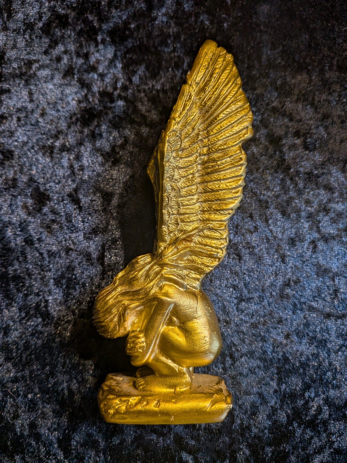 Gold-painted angel figurine with large feathered wings, crouching pose, photographed on dark velvet background - uncanny charity shop object discussed in Tarot DMs interview on haunted objects and folklore. Gold-painted angel figurine with large feathered wings, crouching pose, photographed on dark velvet background - uncanny charity shop object discussed in Tarot DMs interview on haunted objects and folklore.