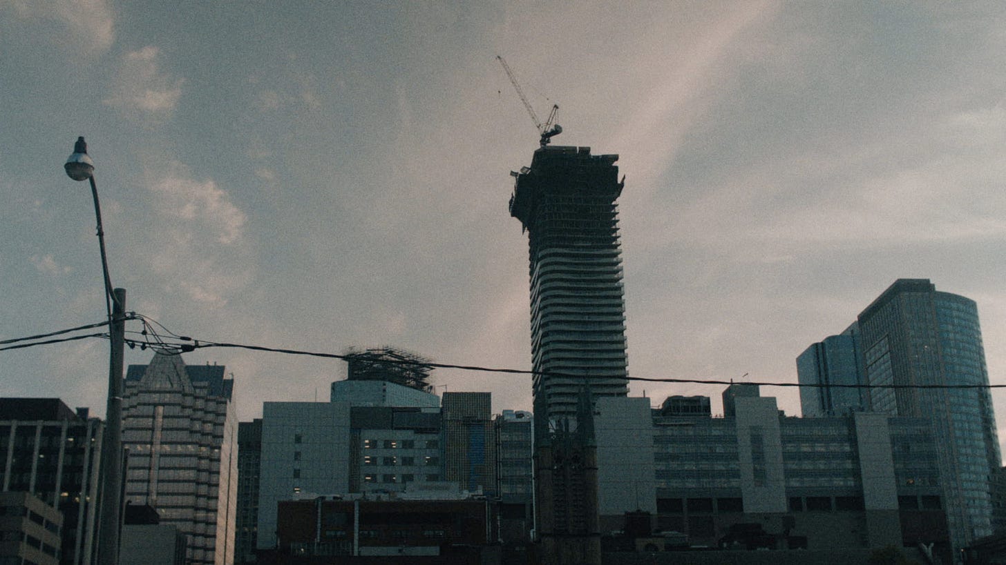 Dark city skyline with a tall high-rise under construction beneath a cloudy sky.