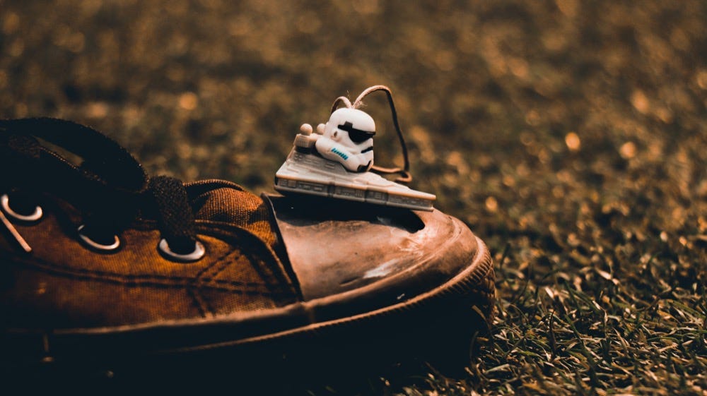 Na zdjęciu stare buty, na trawie, z figurka szturmowca z Gwiezdnych Wojen na nosku.