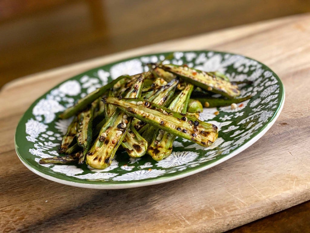 Charred okra, made on a stovetop grill or griddle, on a green-and-white plate. The recipe is from Cooks Without Borders.