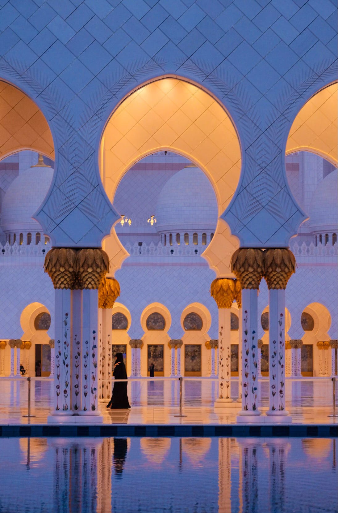 Grand mosque arches reflecting in still water under deep blue evening light