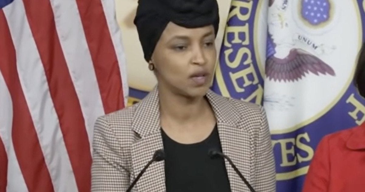 Ilhan Omar speaking at a press conference with the American flag in the background, addressing important political issues.