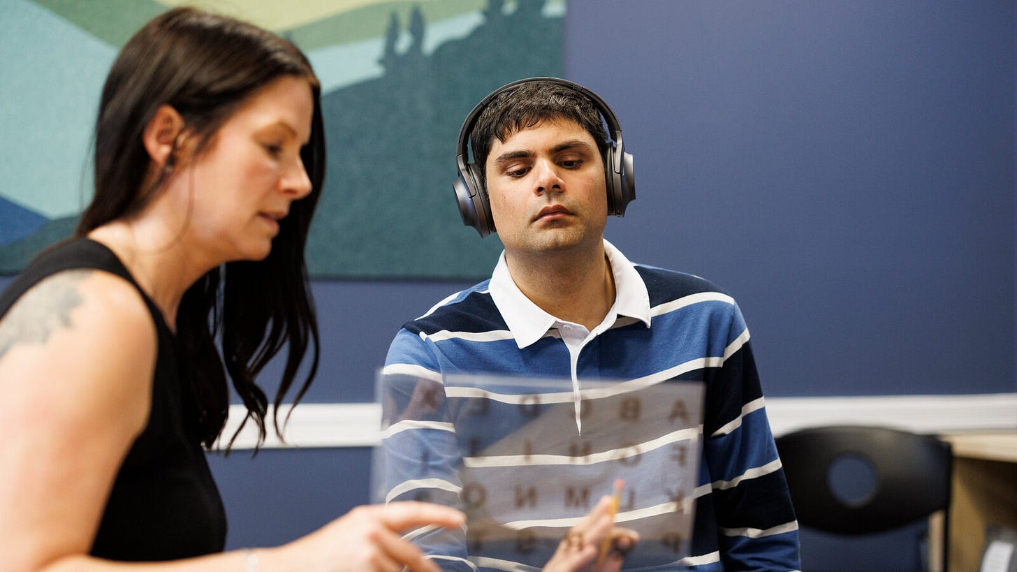 A young man in headphones focuses on a clear letterboard held up by a practitioner A young man in headphones focuses on a clear letterboard held up by a practitioner