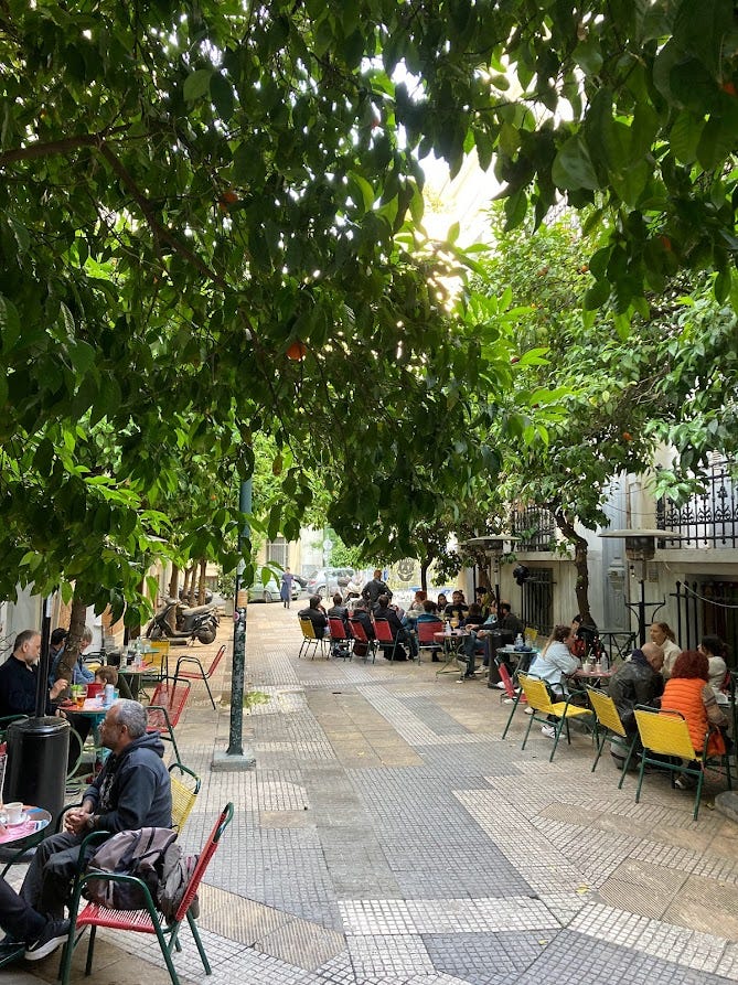 beautiful little street with many green trees in athens, many street cafés, people sitting outside
