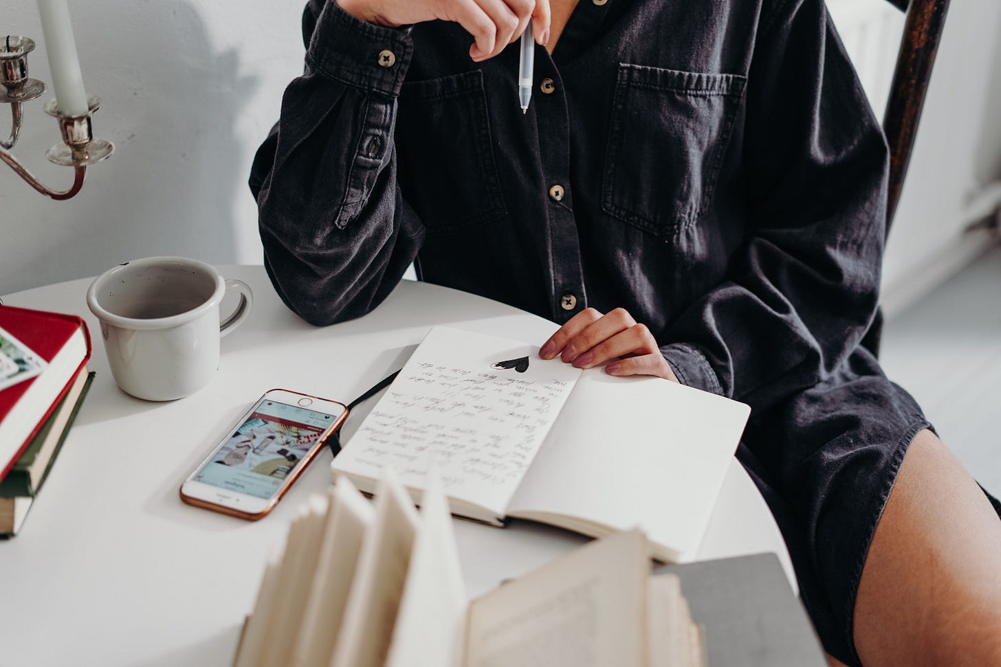 woman writing with coffee at table surrounded by books and her phone woman writing with coffee at table surrounded by books and her phone