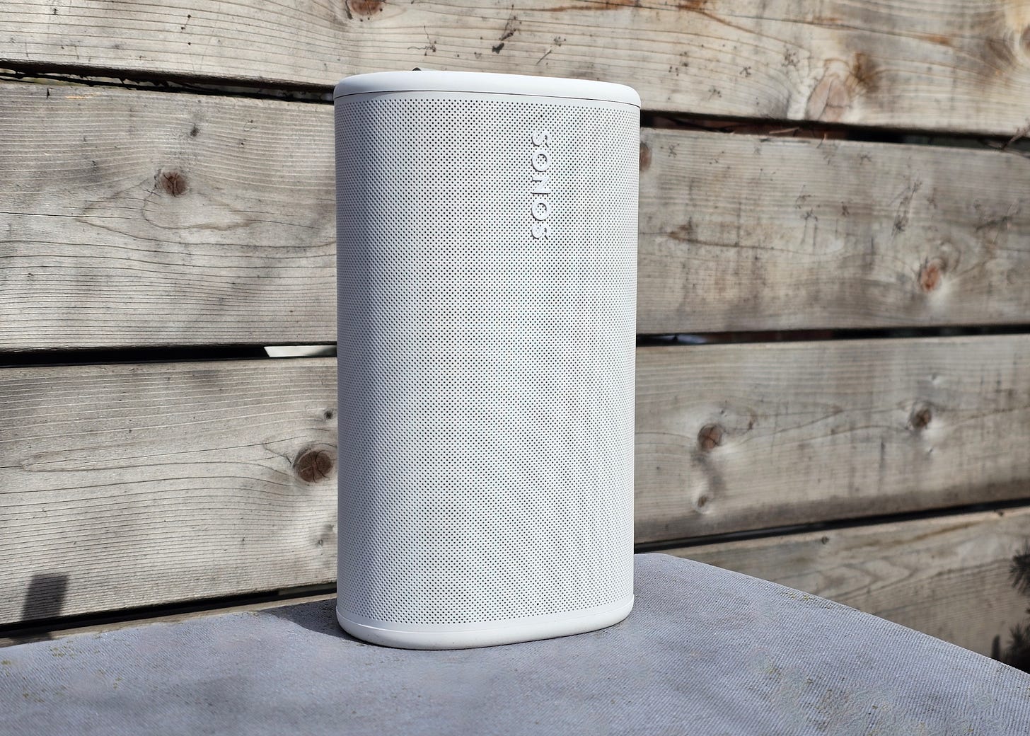 A white Sonos Play sitting in front of a fence. A white Sonos Play sitting in front of a fence.