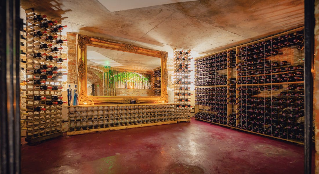 A wine cellar with wines on racks on the walls, a golden framed mirror, and a red floor A wine cellar with wines on racks on the walls, a golden framed mirror, and a red floor