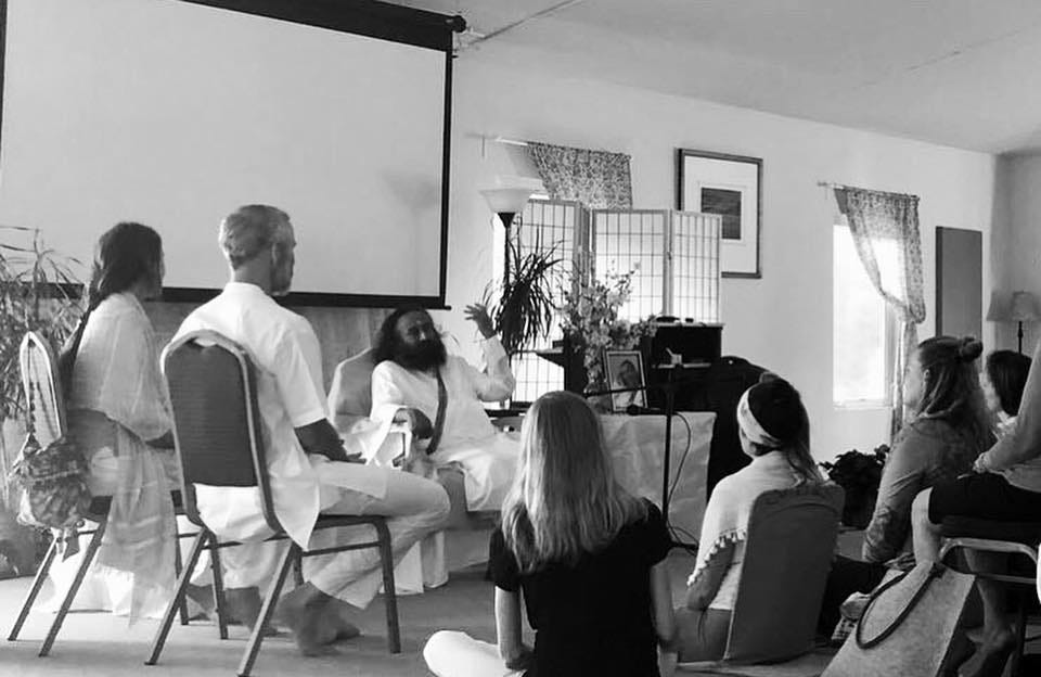 black and white image of Sri Sri Ravi Shankar speaking in front of an audience. The author is pictured seated in the front row.