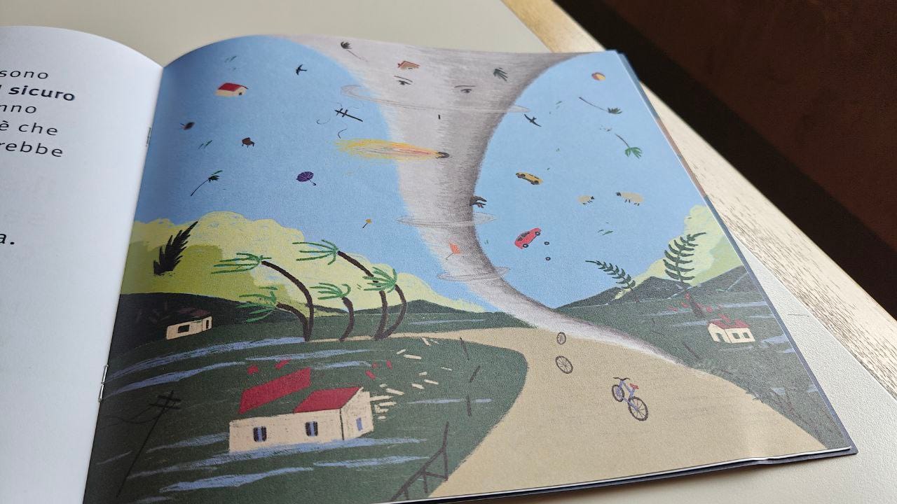 Pagina aperta della Scatolina URAGANO edita da efffequ e illustrata da Kita. Illustrazione a colori di un tornado a imbuto che attraversa un paesaggio. Il vortice di vento solleva in aria oggetti vari come auto, alberi, una bicicletta e una casa, mentre a terra si vedono alberi piegati e detriti.