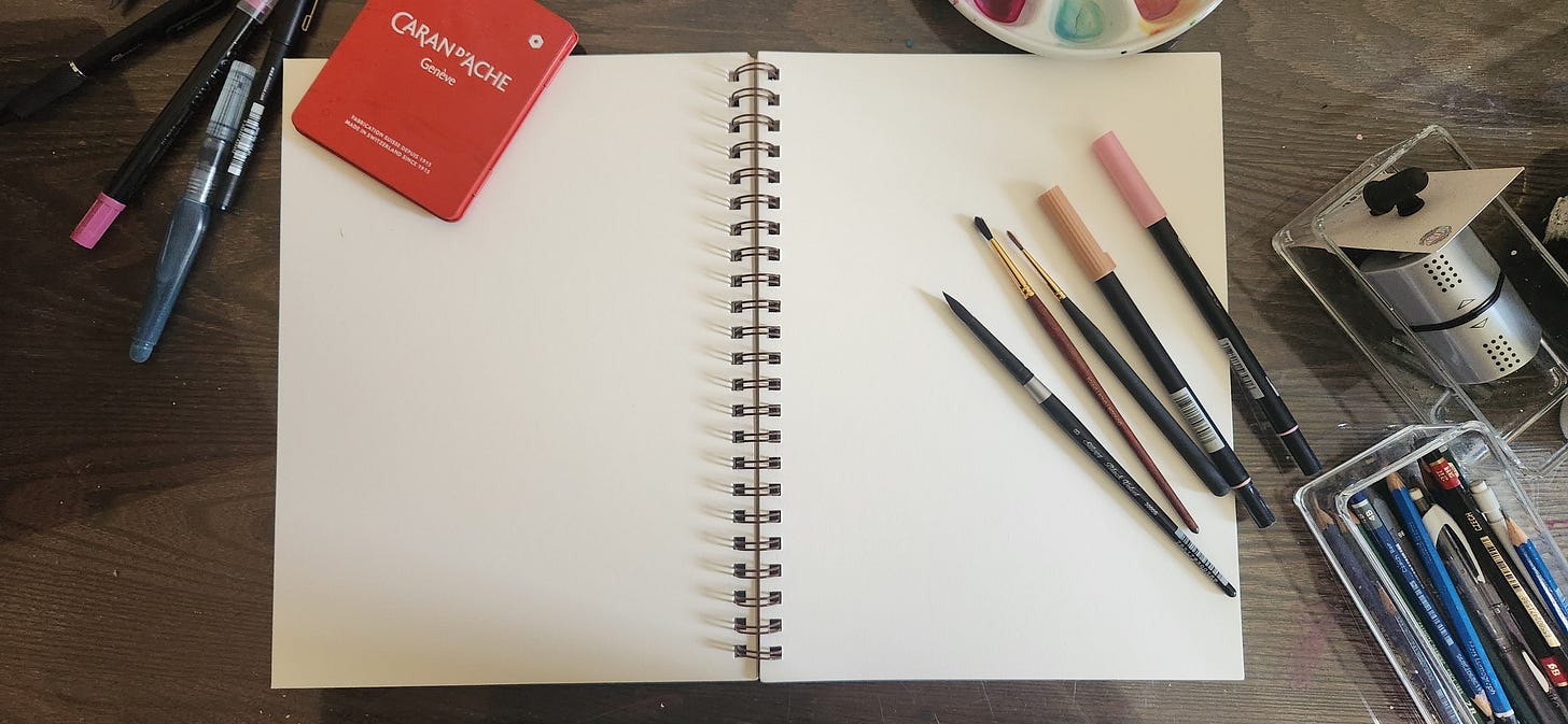 A spiral-bound sketchbook opened to a blank page on a dark wood desk. The sketchbook is surrounded by paintbrushes, pencils, markers and pastel crayons. A spiral-bound sketchbook opened to a blank page on a dark wood desk. The sketchbook is surrounded by paintbrushes, pencils, markers and pastel crayons.