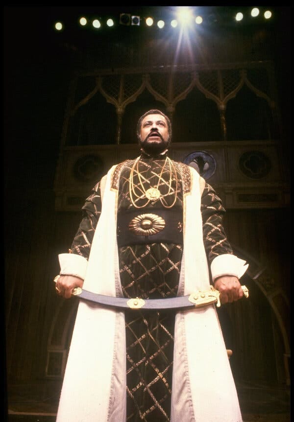 A production images of James Earl Jones as Othello. He is dressed in a long black and gold robe and he is holding a sword.