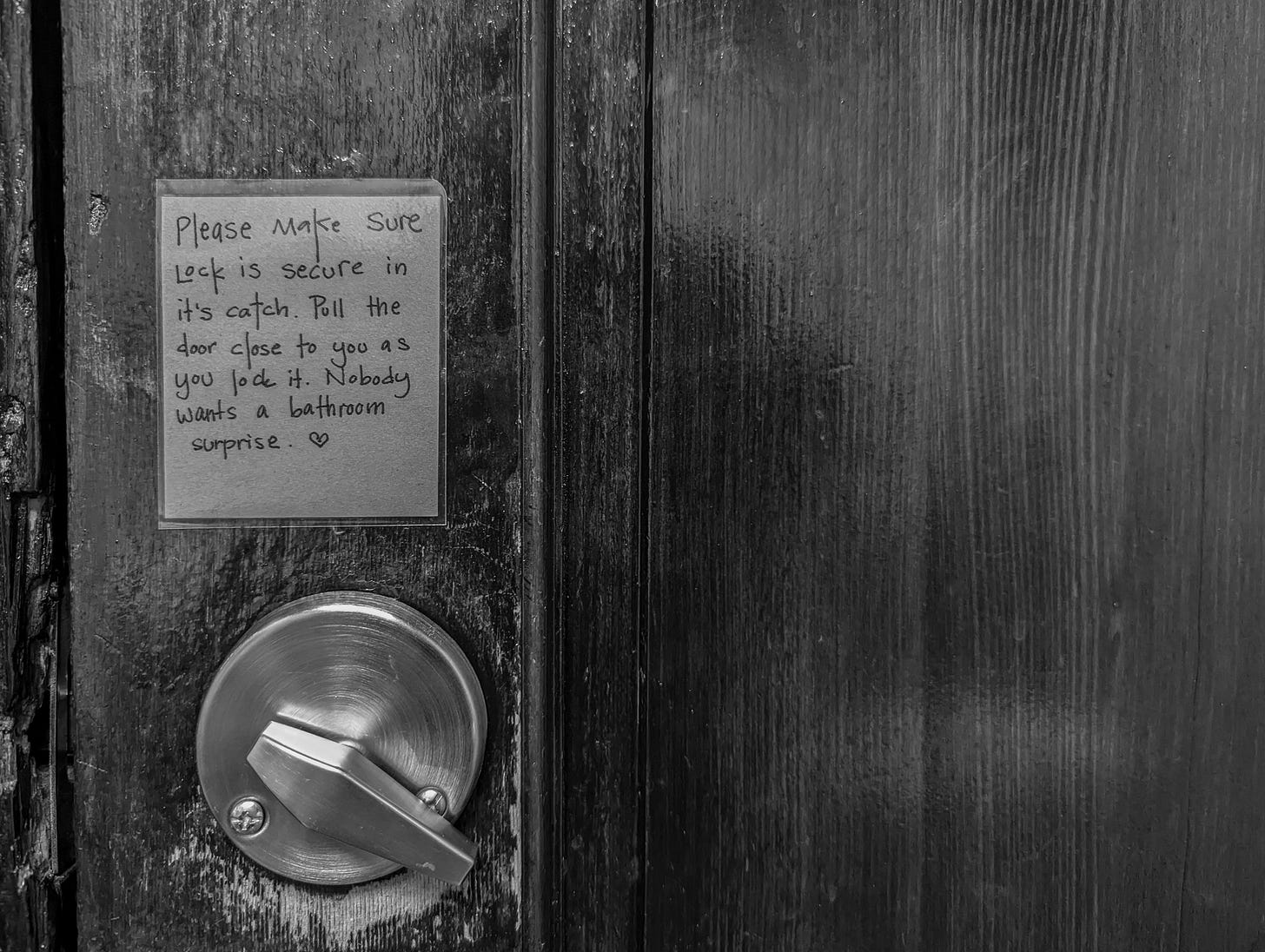 Photo of a note above a bathroom door lock. The note reads: Please make sure lock is secure in its catch. Pull the door close to you as you lock it. Nobody wants a bathroom surprise (heart).