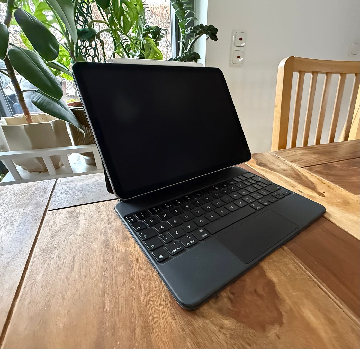 iPad Pro attached to Magic Keyboard case on wooden table, laptop-style setup for productivity and typing.