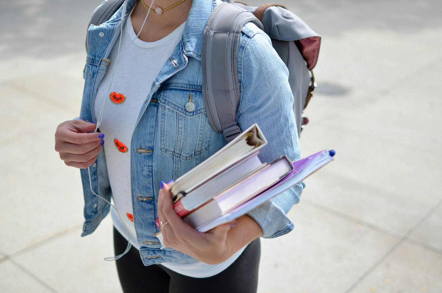 Student holding three books in one hand with a backpack on thier back.