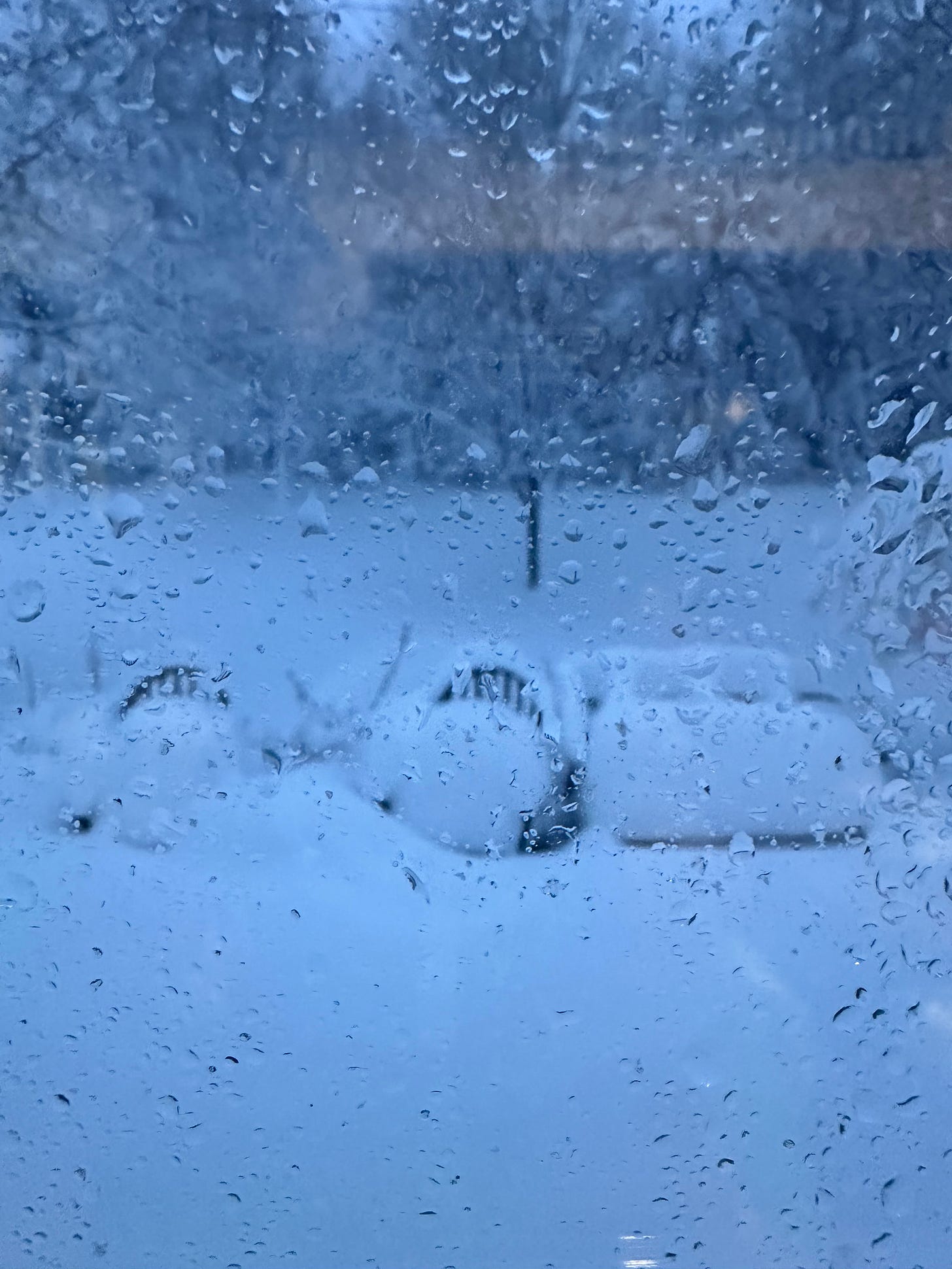 seen through a glass pane with droplets of moisture is a thick layer of snow on patio furniture