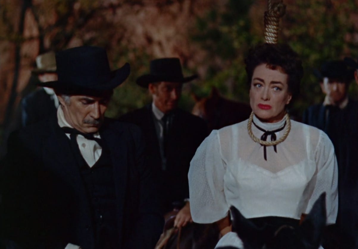 A screenshot from the movie Johnny Guitar. Joan Crawford in a white dress and red lipstick has a noose around her neck, while several men in black hats and black jackets look dismayed. A screenshot from the movie Johnny Guitar. Joan Crawford in a white dress and red lipstick has a noose around her neck, while several men in black hats and black jackets look dismayed.