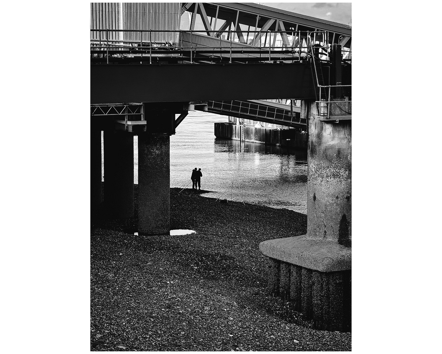 At low tide, underneath the Mersey Ferry terminal, two young men are fishing.