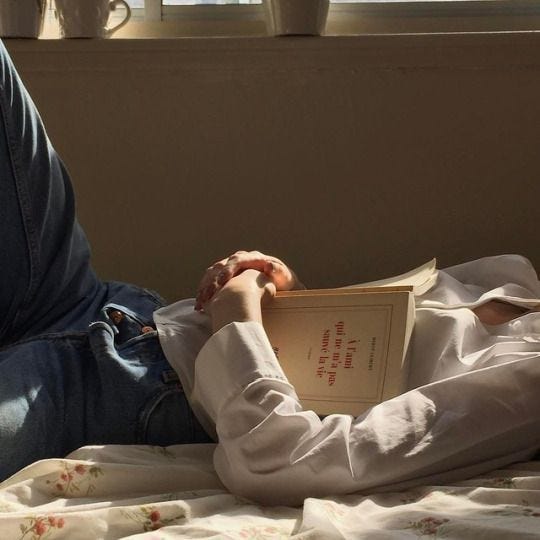 This may contain: a person laying in bed reading a book