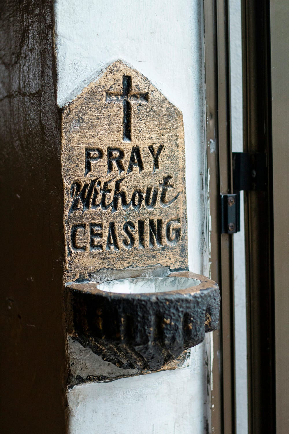 stone holy water font with cross and the words “I pray without ceasing”