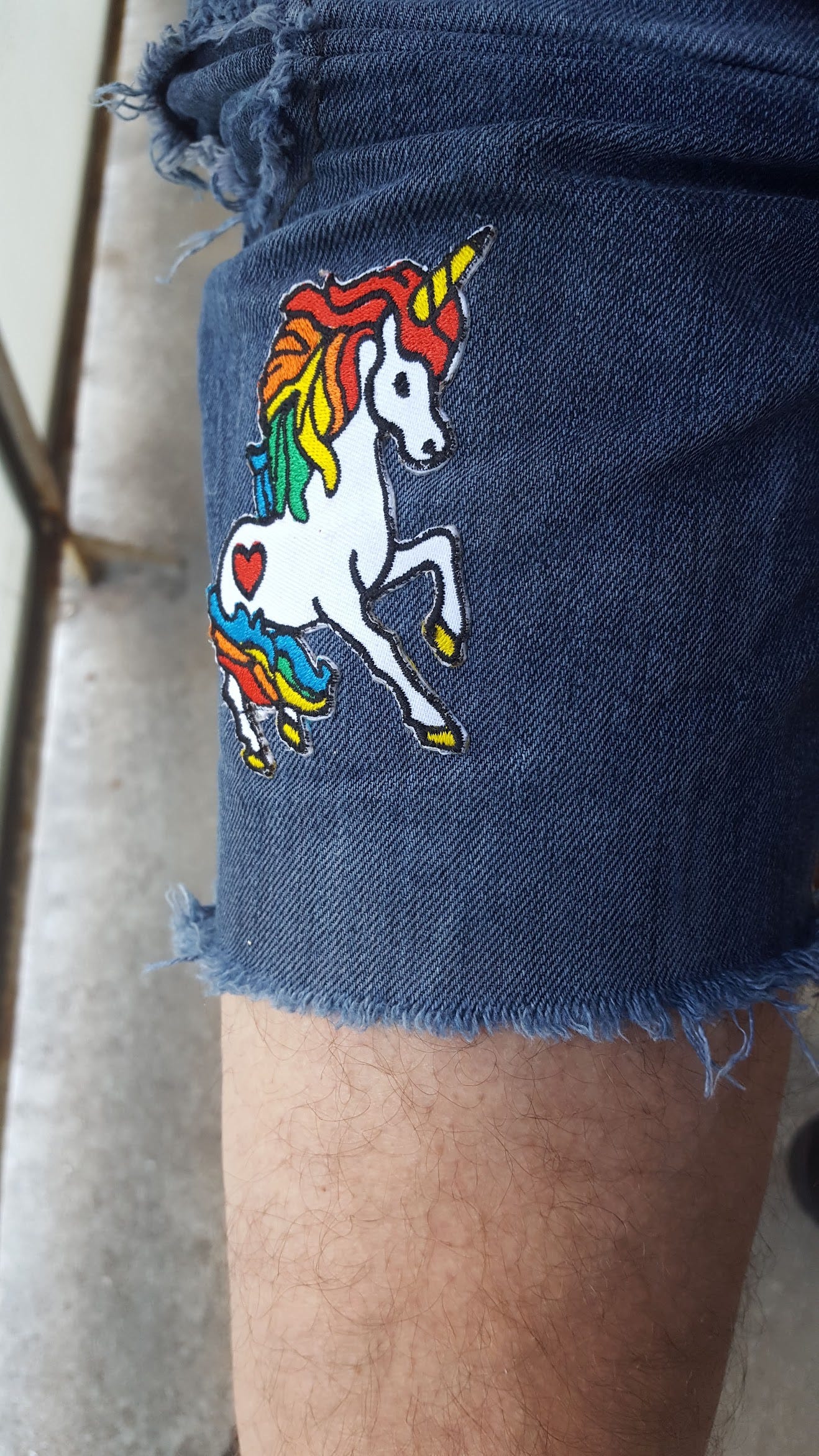 Pictured: Close-up of a Rainbow Unicorn patch sewn to a pair of jeans shorts.