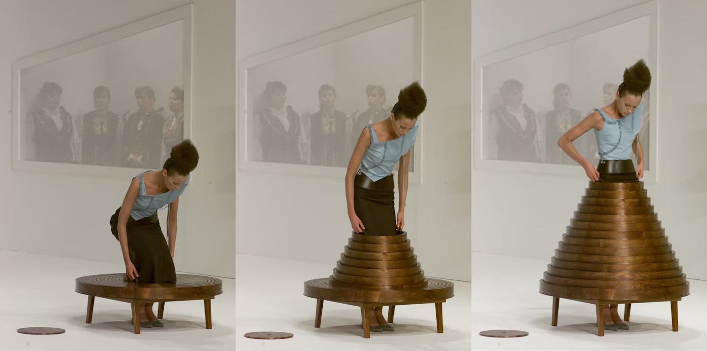 Three-panel image of Hussein Chalayan’s coffee table dress showing a model stepping into a wooden table structure, lifting it around her waist, and transforming it into a hooped skirt. Three-panel image of Hussein Chalayan’s coffee table dress showing a model stepping into a wooden table structure, lifting it around her waist, and transforming it into a hooped skirt.