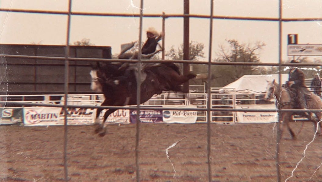 A cowboy riding a bucking bronco. horse is all four hooves off the ground and cowboy is leaning backward. photo taken from stands and shows fence in forground. A cowboy riding a bucking bronco. horse is all four hooves off the ground and cowboy is leaning backward. photo taken from stands and shows fence in forground.