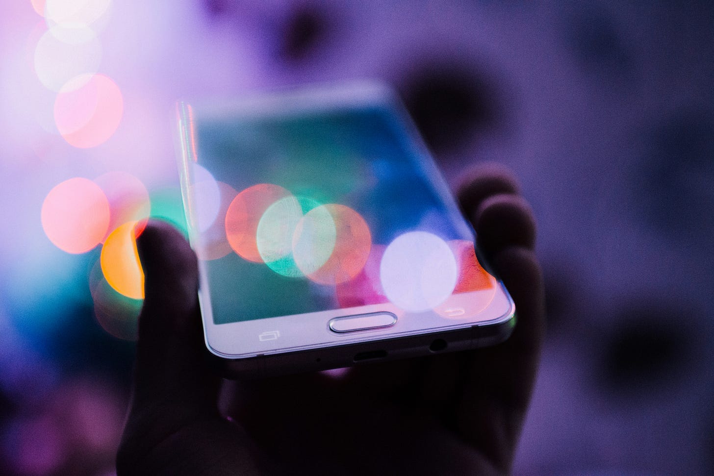 A hand holding a smartphone. There are a bunch of blurry, colored orbs surrounding it.