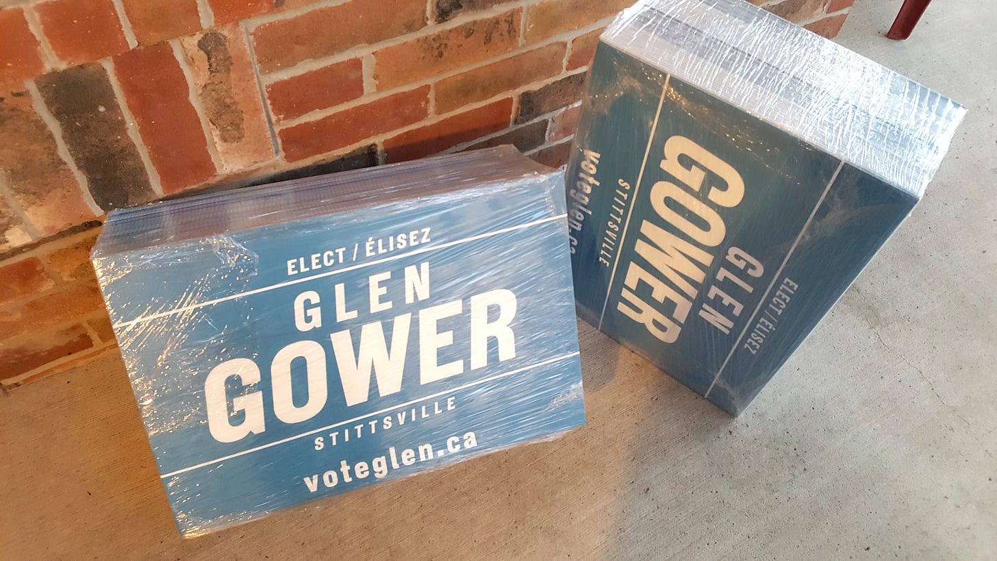 Two stacks of election signs wrapped in plastic, in front of a brick wall