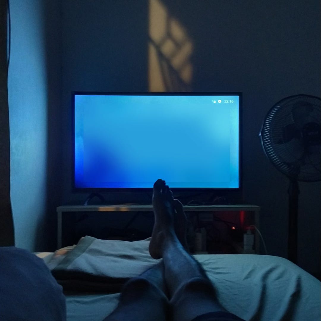 Photo from POV of a person watching TV from their sofa at night. The room is dark and the TV screen is a dark blue. Photo from POV of a person watching TV from their sofa at night. The room is dark and the TV screen is a dark blue.
