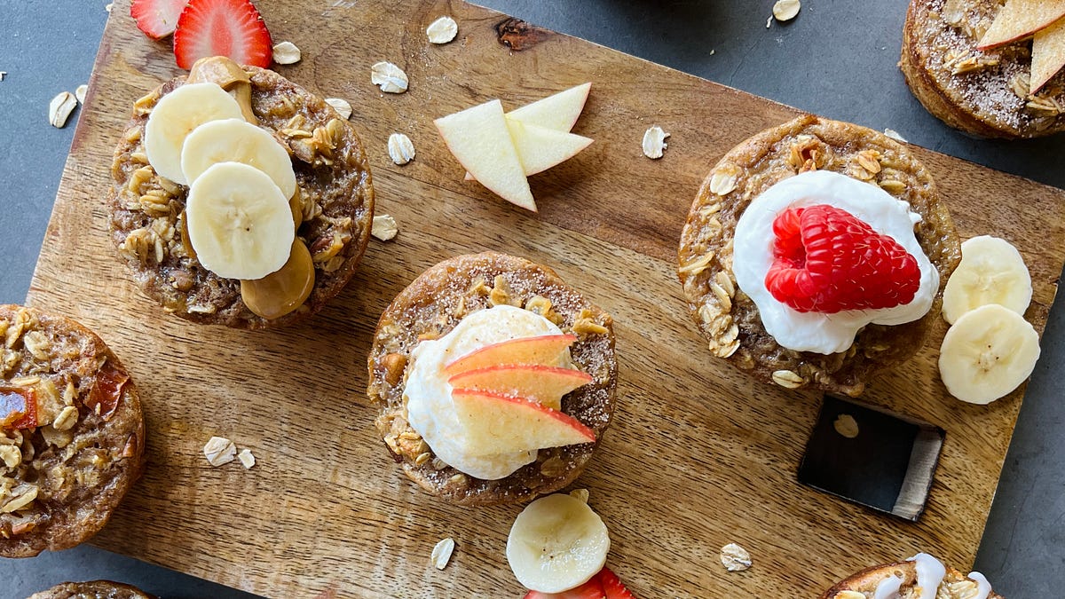 Baked oatmeal cups topped with yogurt and fresh fruit on a wood cutting board.