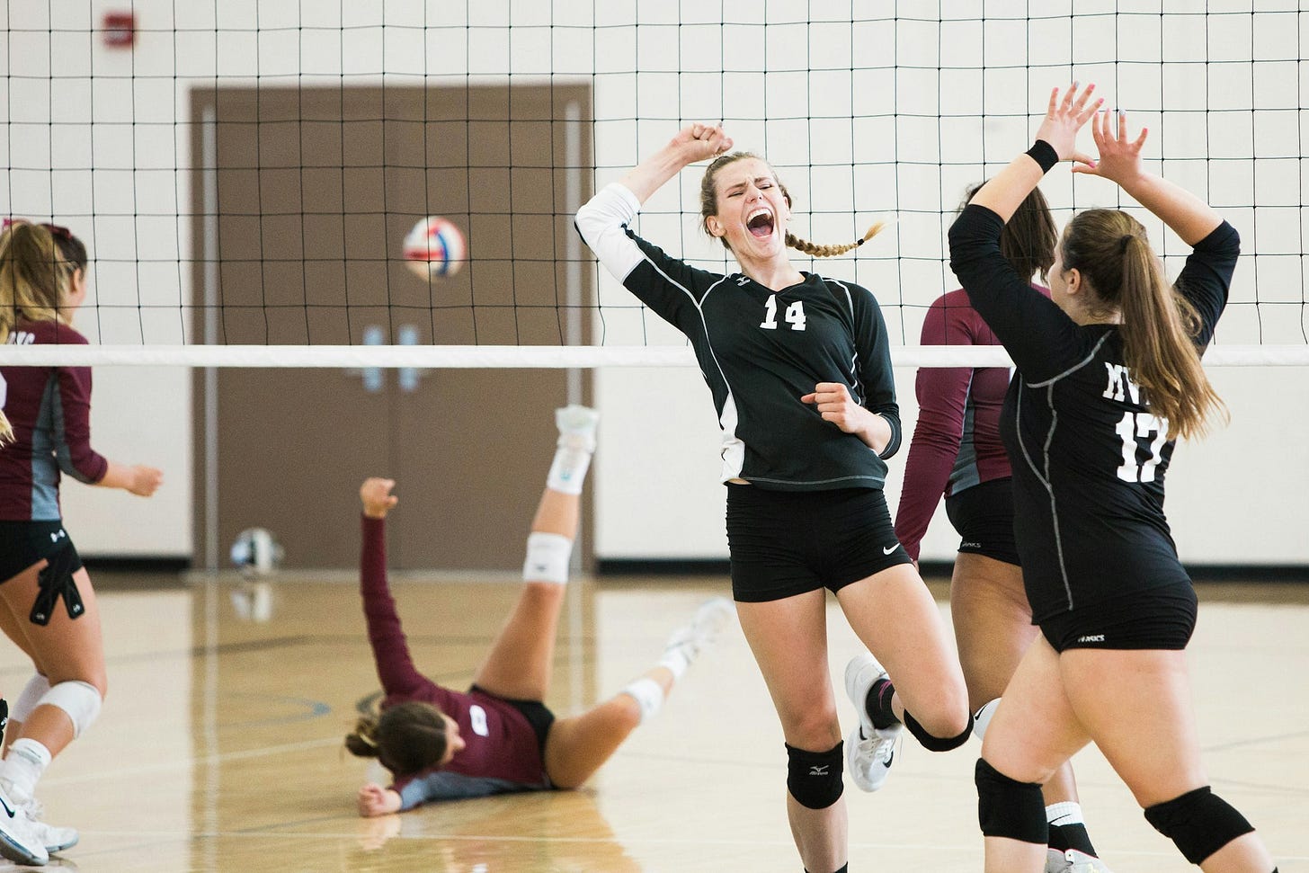 the members of one volleyball team celebrate as an opponent takes a fall