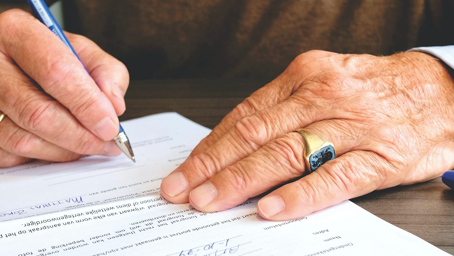 Man with 2 visible hands holding a pen and signing a legal document