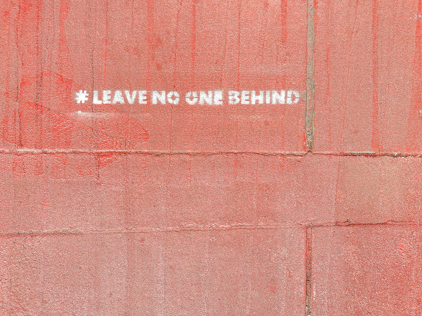 A message painted on a red concrete wall. #Leave No One Behind A message painted on a red concrete wall. #Leave No One Behind