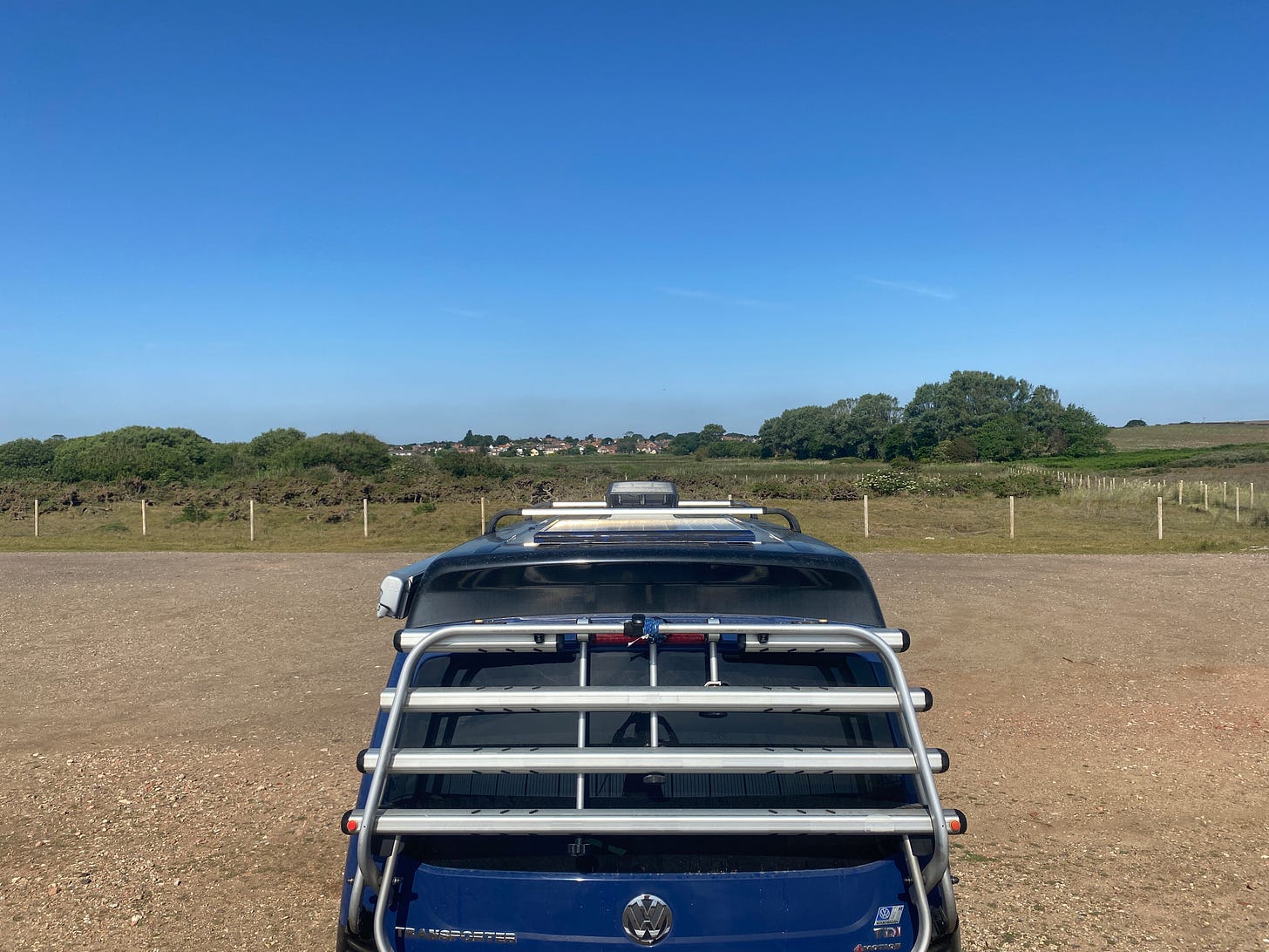 blue campervan parked up overlooking fields and a blue sky