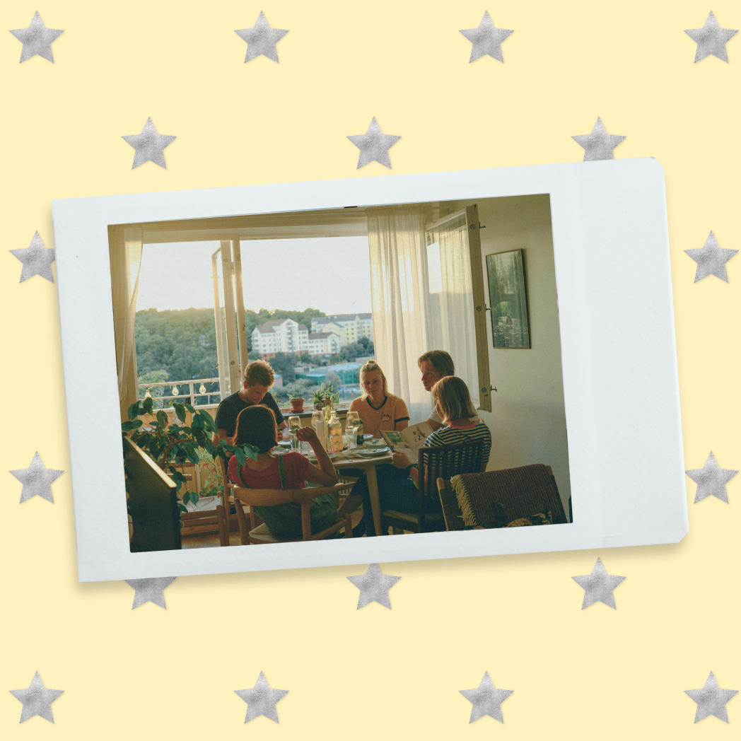 Polaroid-style photo of five people sharing a meal in a sunlit apartment with an open balcony view.