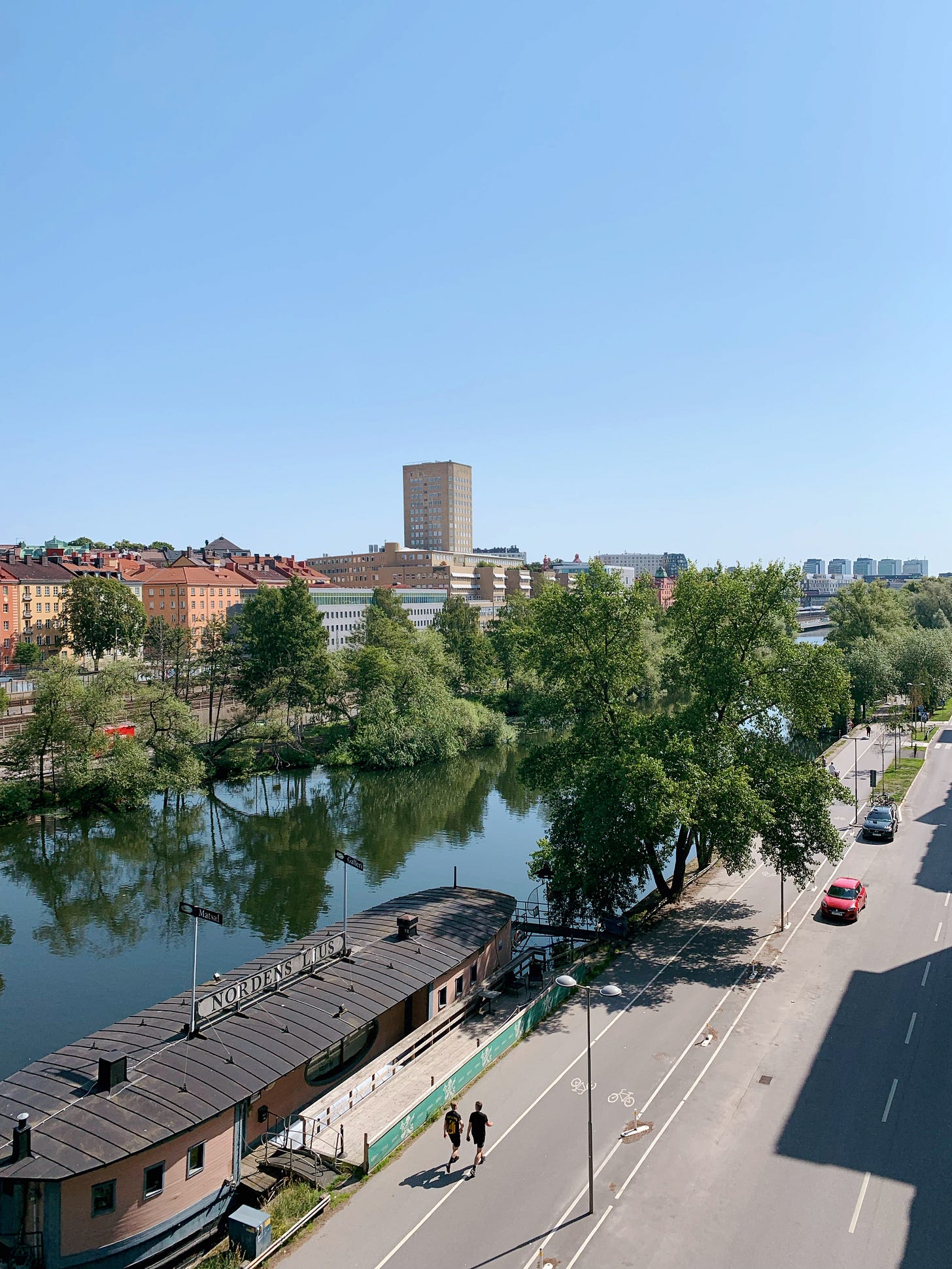 River view from the bridge, with two people walking and a few cars driving on the road