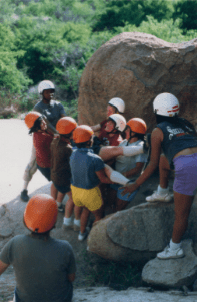A group of people with helmets on climbing rocks.