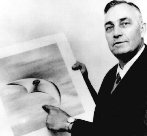 Black and white photo of Kenneth Arnold holding a photo and pointing to an artist's depiction of the UFO he saw.