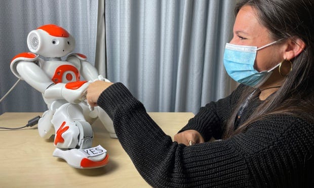 A Nao robot, a humanoid robot about 60cm tall, gives a fist=pump to a woman in a surgical mask A Nao robot, a humanoid robot about 60cm tall, gives a fist=pump to a woman in a surgical mask