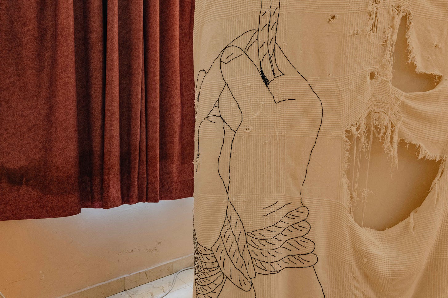 A torn quilt with a stitching of tied hands with curtains in the background