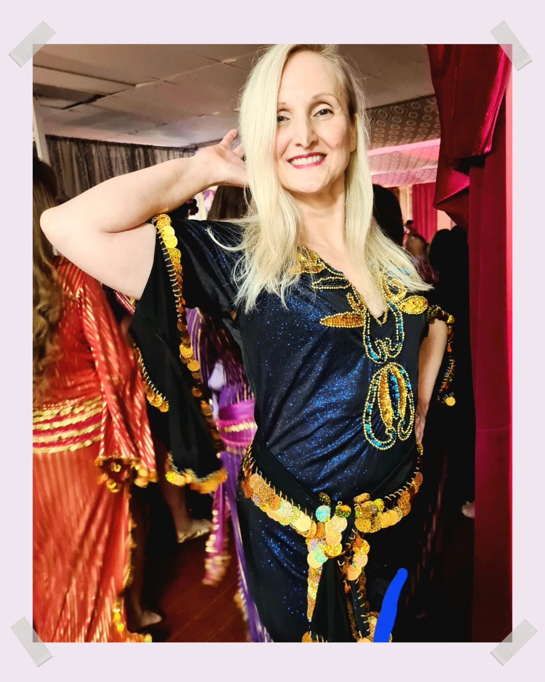 Belinda stands with one hand behind her head, the other on her hip. She's smiling brightly in a bellydancing outfit
