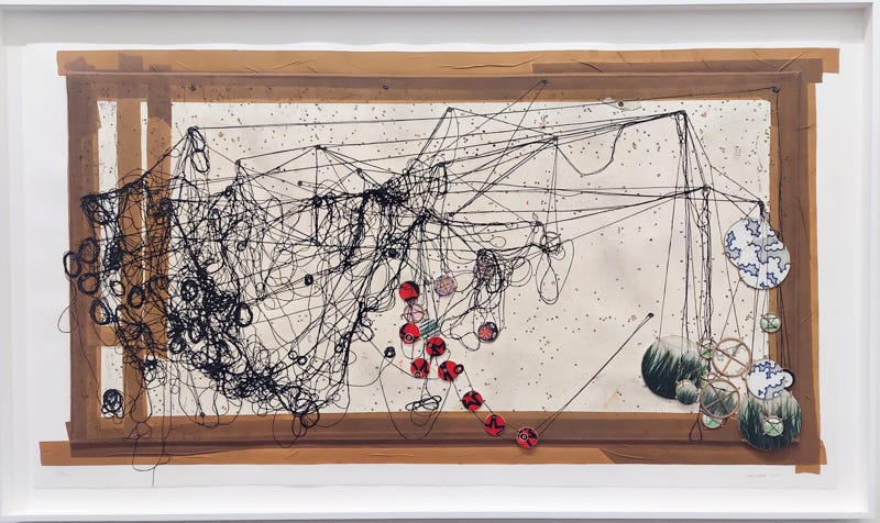 A work of abstract art made from loops of black string and colorful printed paper cut into circles on a white background with a brown wood frame