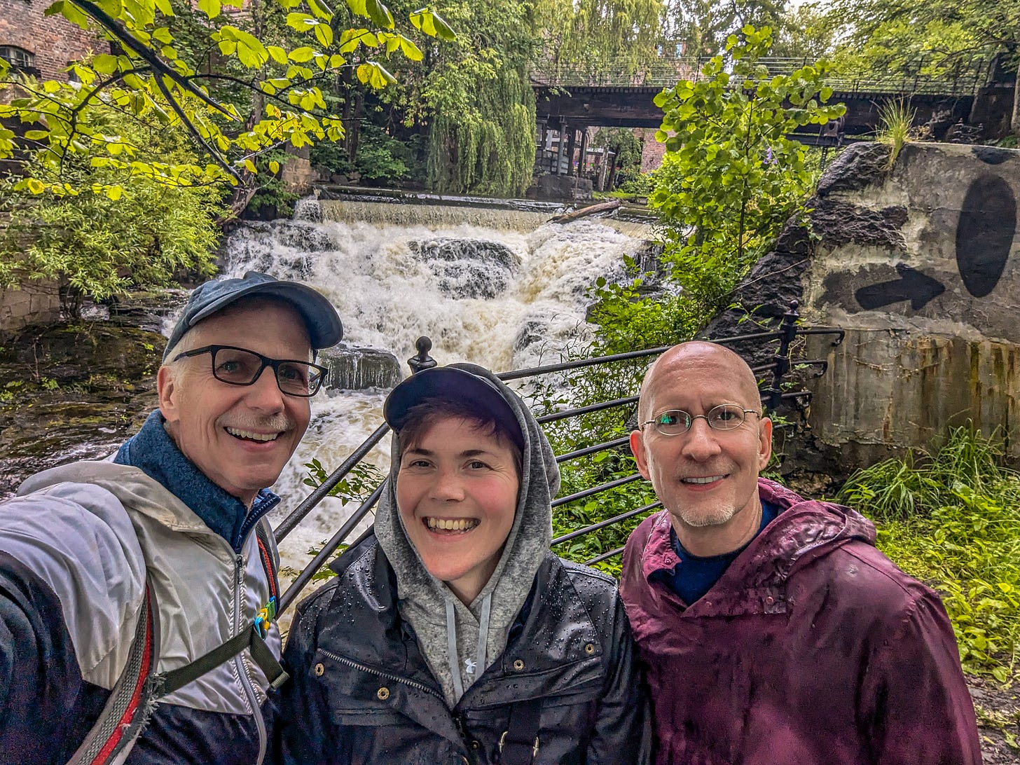 Michael, Marianne, and Brent standing in the rain in front of a waterfall. 
