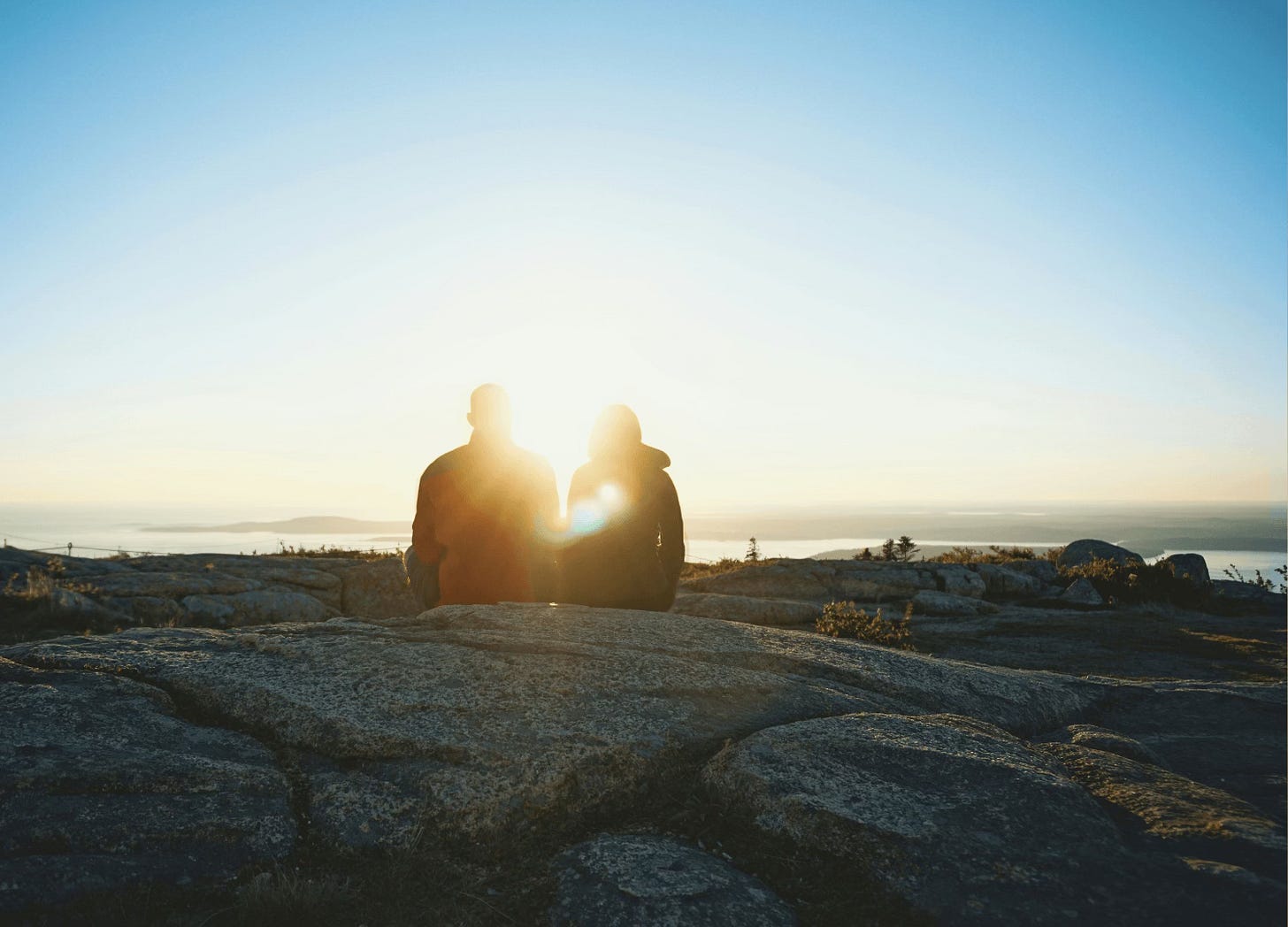 Two people in silhouette sitting on rocks overlooking the sea Two people in silhouette sitting on rocks overlooking the sea