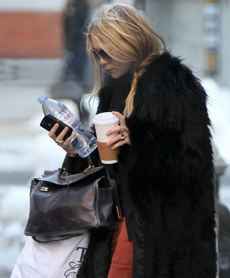 This may contain: a blonde woman in black coat and red pants holding a coffee
