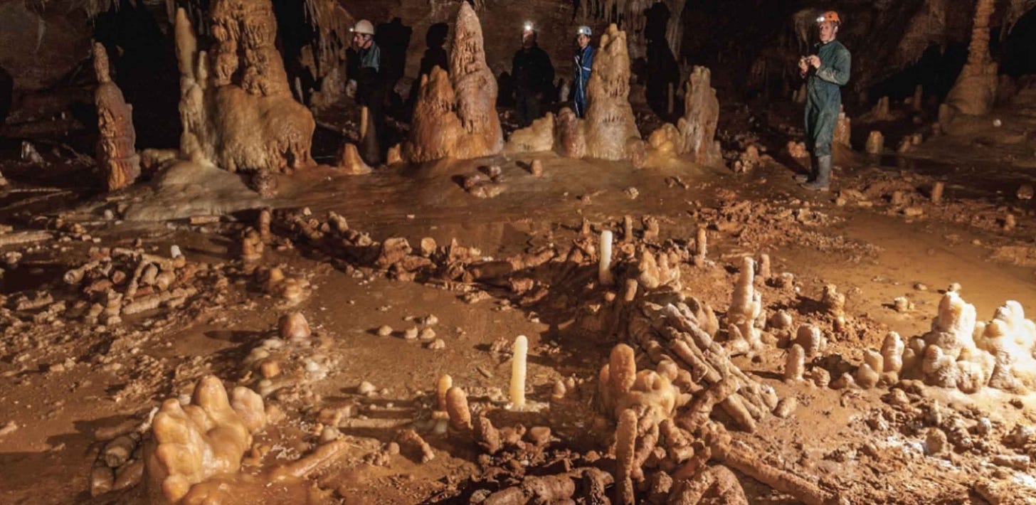 Image deep inside a cave with stalagmites on cave floor forming a circular structure, archaeologists in helmets visible