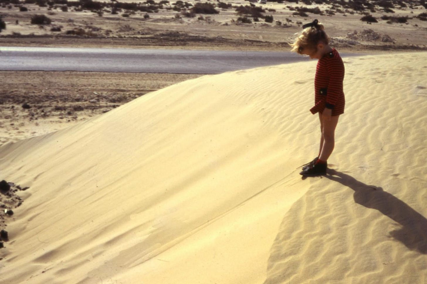 A young girl standing on top of a sand dune