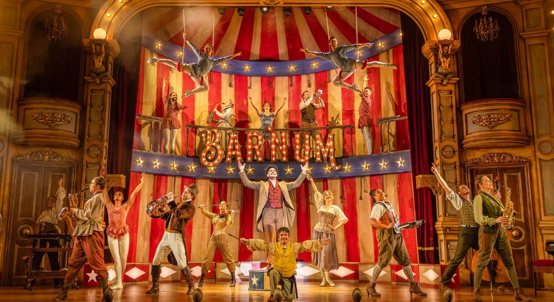 A group of circus performers on a stage with a red and white backdrop and ornate pillars