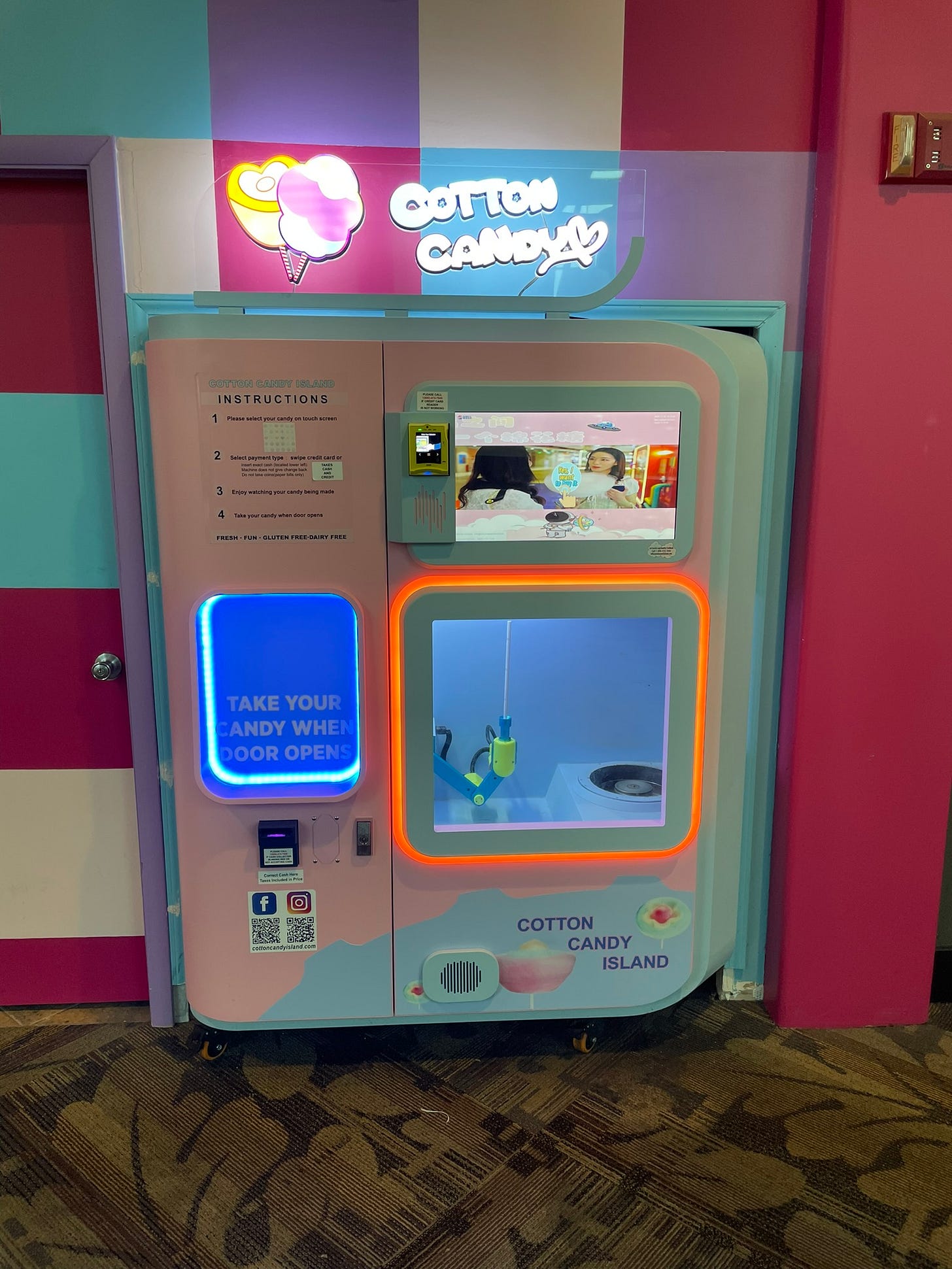 A pink and blue, neon lighted automatic cotton candy vending machine.